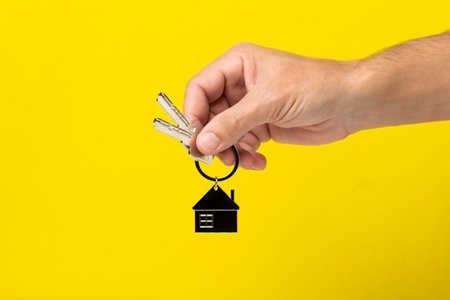House key with keychain in hand isolated on yellow background. Real estate concept.の写真素材