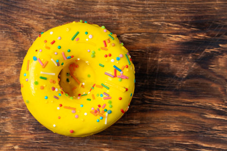 Yellow donut with colorful sprinkles on wooden background. Top viewの写真素材