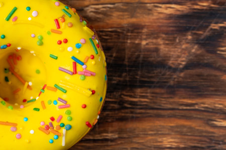 Yellow donut with colorful sprinkles on wooden background. Top view.の写真素材