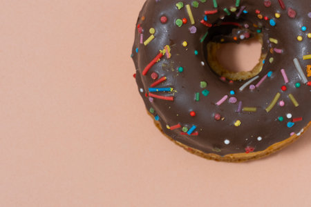 Donut with chocolate icing and colorful sprinkles on pink background.