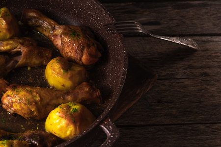 Roasted chicken legs with potatoes in a frying pan on wooden backgroundの写真素材