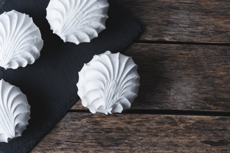 White meringues on a black slate plate on a wooden background