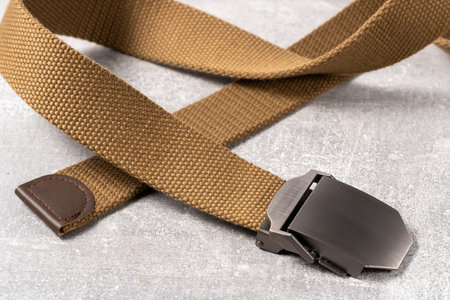 A brown canvas belt with metal buckle on gray background. Closeup.の写真素材