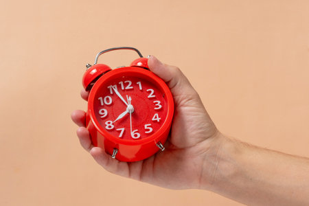 Red alarm clock in hand on a beige background. Time conceptの写真素材