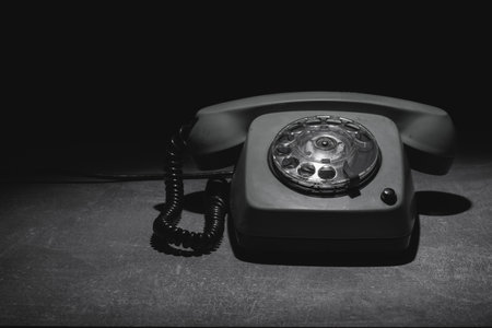 An old rotary phone rests on a dark surface illuminated by soft light, highlighting its classic design. The phone evokes nostalgia and represents a bygone communication era.の写真素材