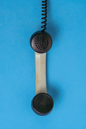 A classic telephone receiver in a neutral tone is placed on a bright blue surface, showcasing its...