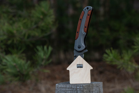 Hunting knife with wooden house on stump in forest. Concept of caring for nature.