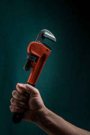 Adjustable pipe wrench in male hand on dark green background.の写真素材
