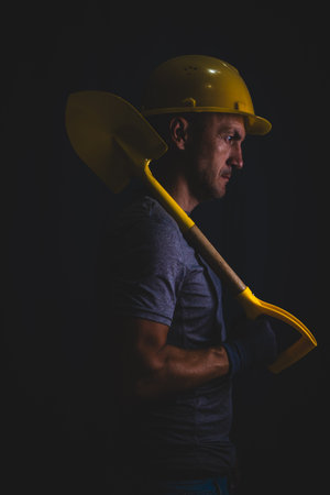 Portrait construction worker in helmet with shovel on  black background.