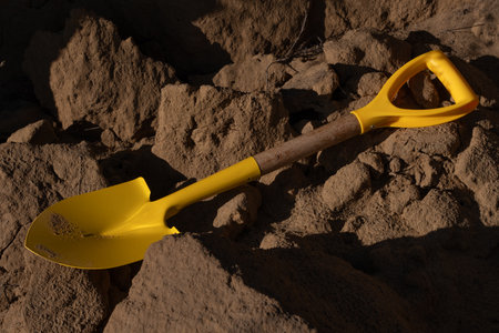 Yellow spade in sand on background brown soil.