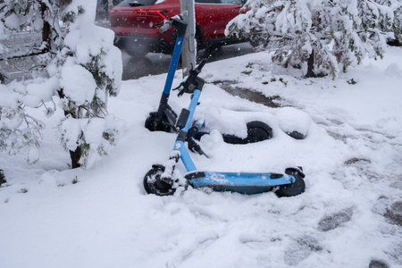 Two abandoned electric scooters in snow by road.の写真素材