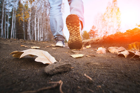 Man walking on road in autumn forest with fallen leaves, close up.