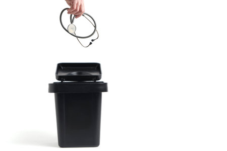 Hand throwing medical stethoscope into trash, representing career change or system failureの写真素材