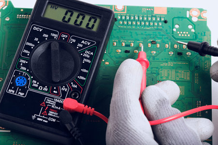 Electronic technician with digital multimeter, close-up. Electronic equipment.