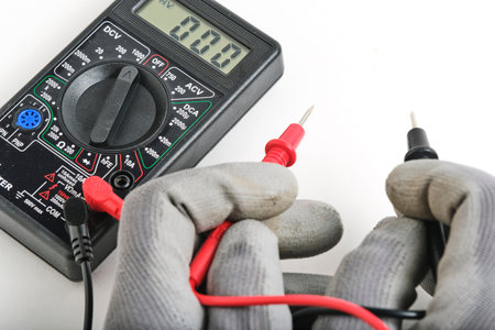 The hands of the electrician with a multimeter on a white background