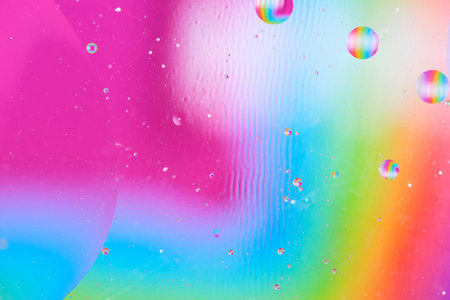 Artistic abstract liquid art with oil drops on pink, blue and green blurred background