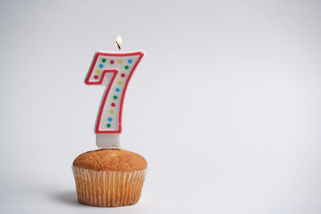 Birthday cupcake with number 7 burning candle on white background