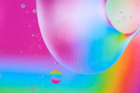 Macro view of large oil sphere on colorful rainbow background with liquid distortion