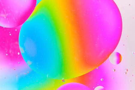 Abstract macro shot of large, colorful oil bubbles floating on water surface with vibrant rainbow gradient background of blue, green, and pinkの写真素材