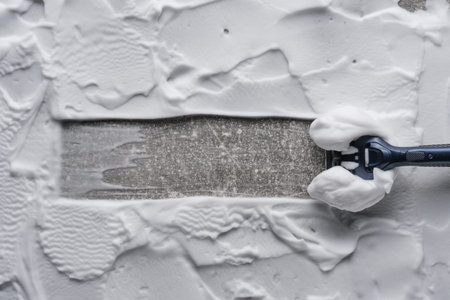 Razor shaving off foam applied to textured gray surface. Clear strip of cleaned space is visible. Concept of effective hair removal or surface cleaningの写真素材