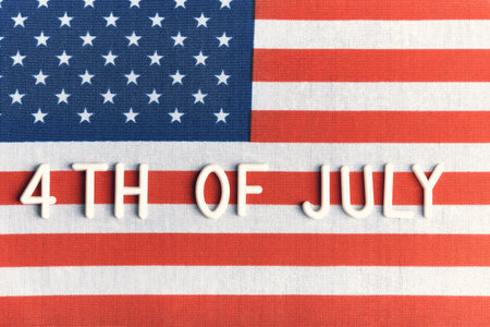 Close up view raised 3D text 4th July resting on textured American flag surface