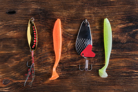 Flat lay four different types fishing lures two metal spoons and two soft plastic baits arranged on...
