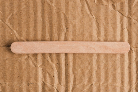 Wooden stick on ribbed corrugated cardboard background. Contrast of smooth and rough textures