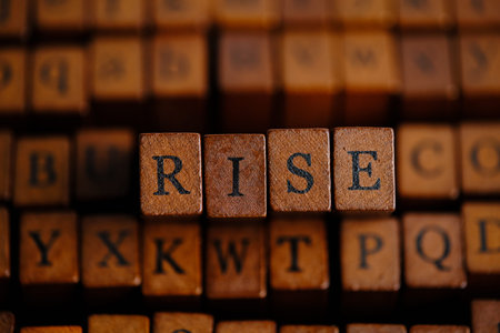 Close up wooden letter blocks spelling RISE against blurred background various alphabet stamps