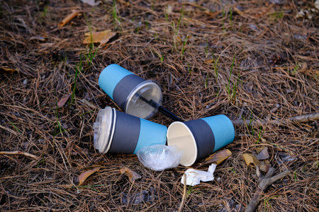 Three discarded blue and black disposable coffee cups lying as litter on dry forest floor