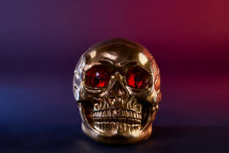 golden skull with scarlet eyes blue and red background close upの写真素材