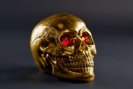 golden skull with scarlet eyes dark background close up with reflexesの写真素材