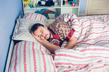young guy with a beard is sleeping in his bedroomの写真素材
