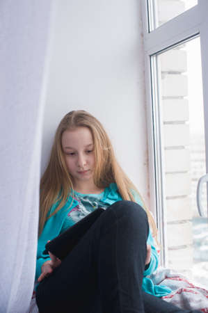 teenage girl sitting on window and looking at the tabletの写真素材