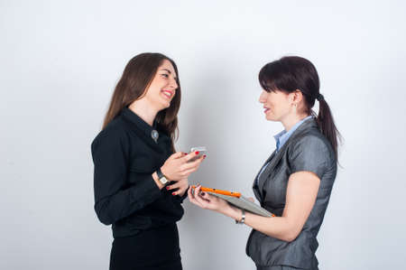 Two business women standing facing each other, holding your phone or tablet and smilingの写真素材