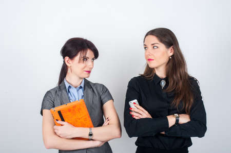 Two business women standing on a light background with your arms crossed and holding a tablet and phone. Looking at each otherの写真素材
