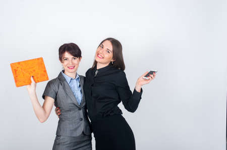 Two business women standing and embracing each other joyfully waving hands, holding a tablet and phoneの写真素材