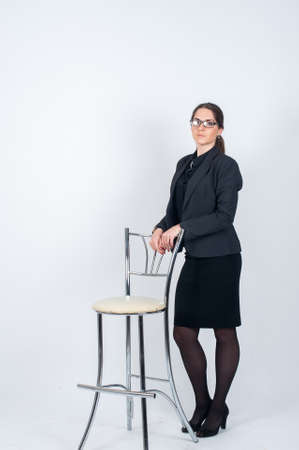 Business woman with glasses standing in the Studio on a light background and put his hands back in his high chair. Vertical photo in full growthの写真素材