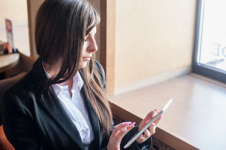 Businesswoman with long dark hair sitting in a cafe near the window and working on the tabletの写真素材