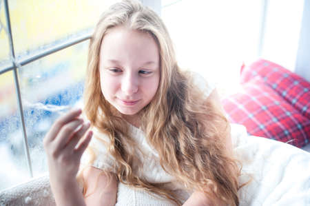 teenager girl sitting near the window and holding a garlandの写真素材