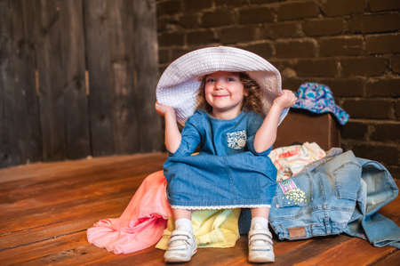 Little girl in white hat sitting in suitcase with things and look at the camera. Traveling with young childrenの写真素材