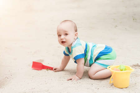 A little boy playing on a white sand. Child with toys for the sandbox. Baby crawling on a sandy beach.の写真素材