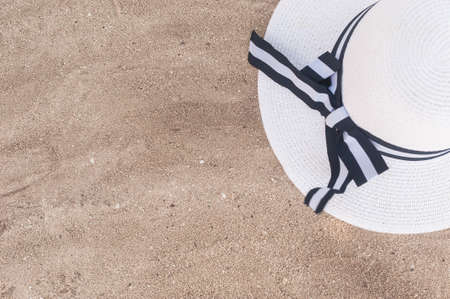 A white hat with wide brim and a seashell lie on the fine light sand. Background with beach accessories.の写真素材