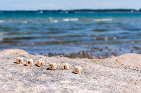 Word Travel on the background of the sea. Letters on wooden cubes on white and sand backgroundsの写真素材