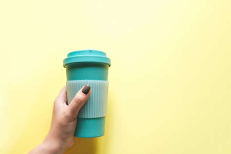 Mint coffee mug in a woman's hand on a yellow background. The concept of waste-free consumption. Concern about the environment, zero wasteの写真素材