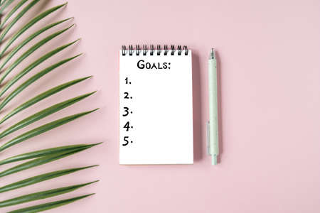 White Notepad sheet with the purposes, stylish pen and a green plant on a pink background. Top view, planning for the yearの写真素材