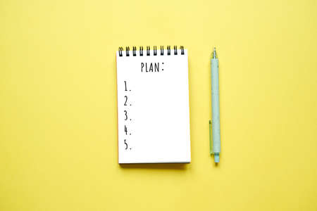 Notepad and pen on yellow background. Drawing up a plan, action points. Flatlayの写真素材