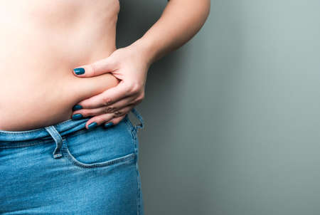 A plump woman in jeans, a fold of skin in her hand. The concept of losing weight by summer.