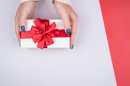 Gift box with a red bow on a gray background in womens hands. Space for the text.の写真素材