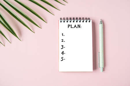 White Notepad sheet with the purposes, stylish pen and a green plant on a pink background. Top view, planning for the yearの写真素材