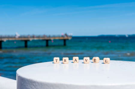 Word Travel on the background of the sea. Letters on wooden cubes on white and sand backgroundsの写真素材